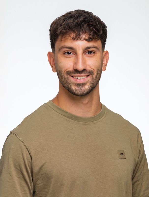 Foto para Casting Pola de estudio de un actor joven sonriendo, con pelo corto oscuro, barba y una camiseta color verde militar sobre fondo blanco.