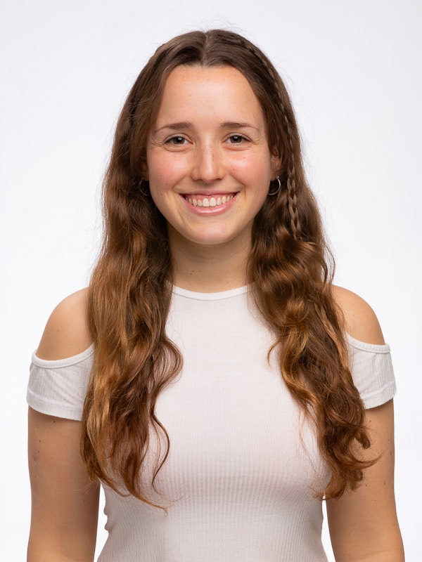 Polas Profesionales Opción A (Recomendada):<br />
Retrato de una mujer joven sonriente con pelo largo castaño y camiseta blanca, foto de estudio tipo pola profesional sobre fondo blanco.